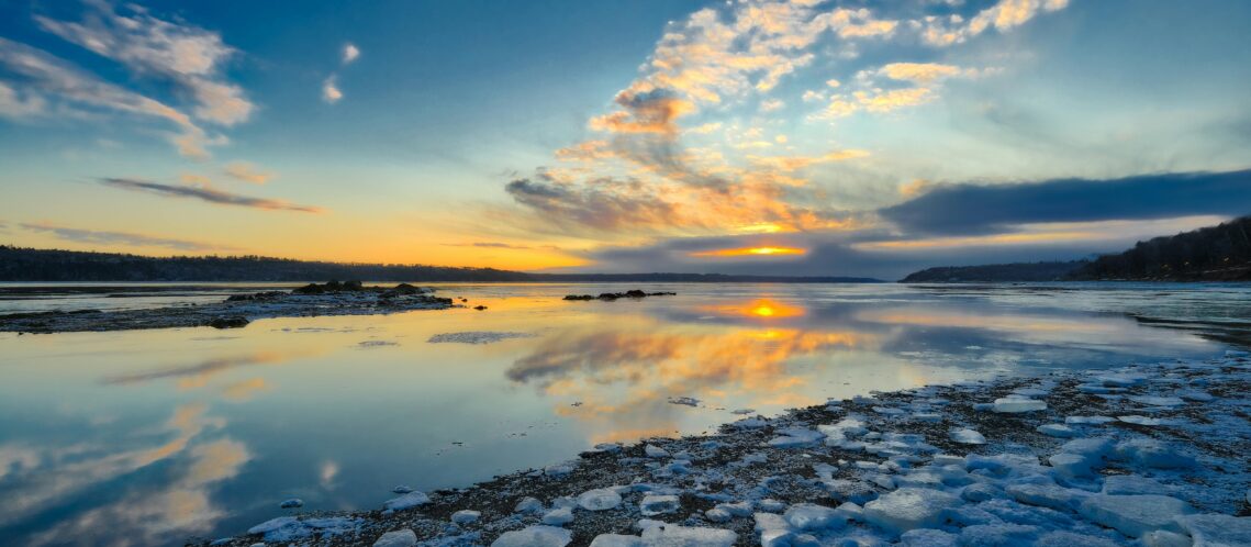 Coucher de soleil hivernal sur un lac au Québec avec reflets colorés dans l’eau calme